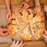 Dziecięce dłonie sięgają po kawałki pizzy z pudełka podczas wspólnego posiłku