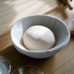 Miska ze świeżym ciastem, obok jajka i mąka na drewnianym blacie