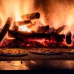 Pizze piekące się w rustykalnym piecu opalanym drewnem z widocznym ogniem