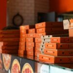Stosy pomarańczowych pudełek na pizzę w pizzerii z ciepłym wnętrzem