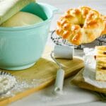 Wyrośnięte ciasto w misce obok świeżo upieczonego chleba i składników