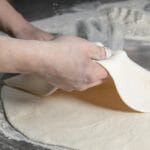 Dłonie formujące kulę ciasta na posypanym mąką blacie