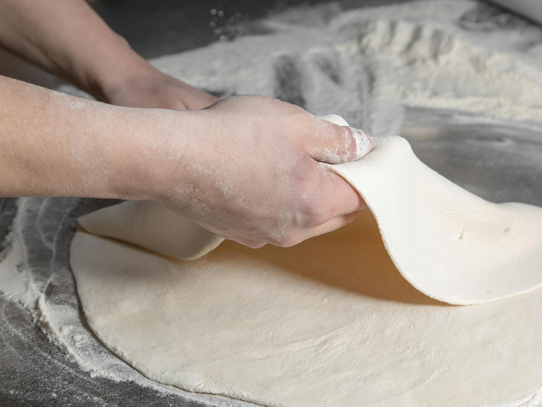 Dłonie formujące kulę ciasta na posypanym mąką blacie
