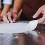 Dłonie formujące kulkę ciasta na pizzę na oprószonym mąką blacie