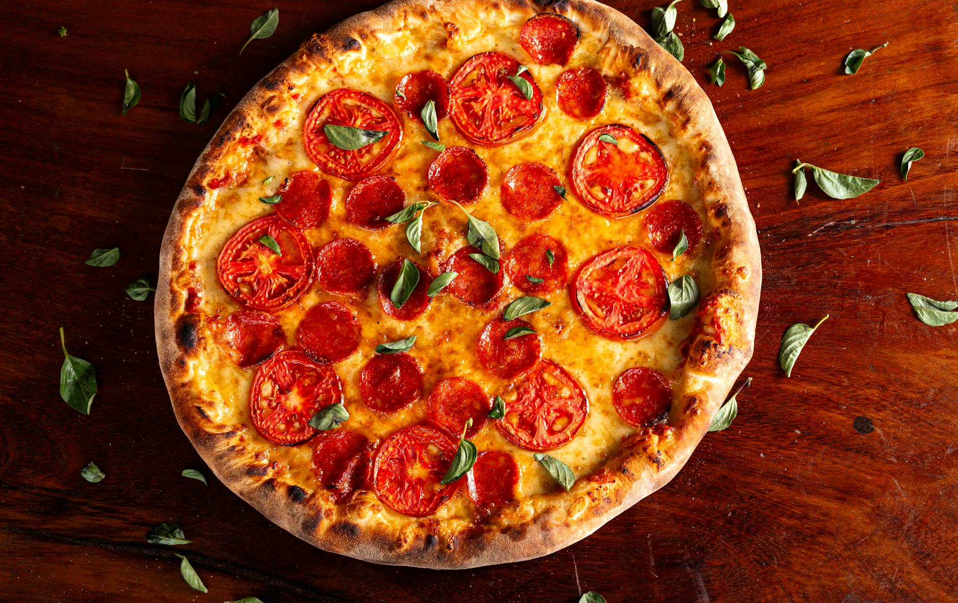 Ranking pizzy z ostrą kiełbasą i chilli: miejsca dla fanów ognia Pepperoni pizza z pomidorami i bazylią na drewnianym stole