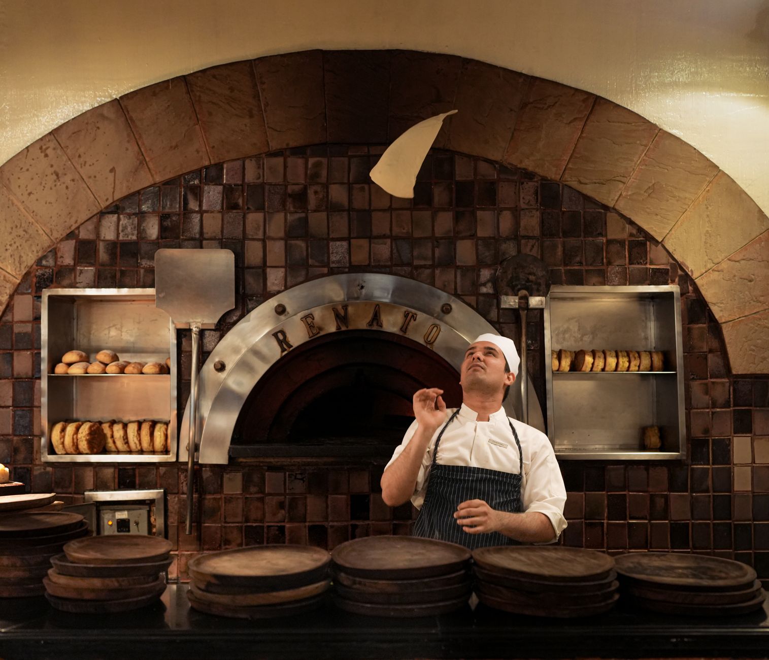 Recenzja pizzerii z opcją bezglutenową: smak, struktura, bezpieczeństwo Pizzaiolo podrzuca ciasto na pizzę w rustykalnej kuchni