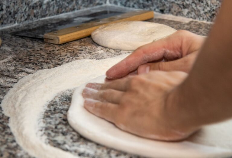 Dłonie zagniatające ciasto na oprószonym mąką blacie kuchennym